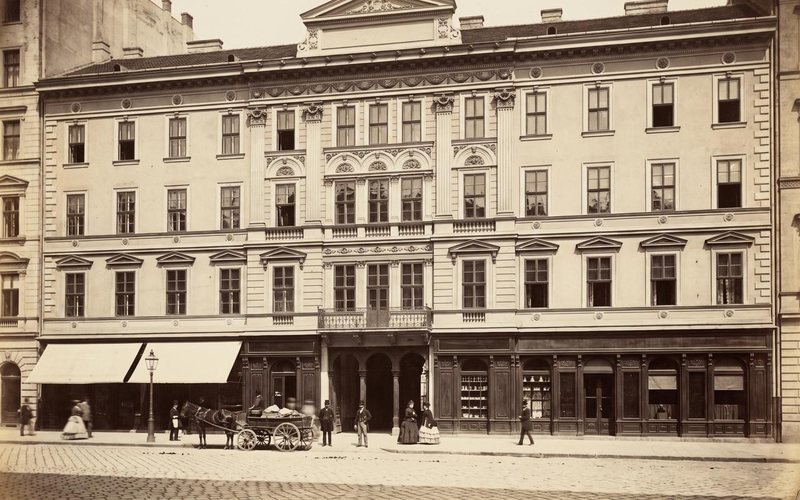 Az épület homlokzata a földszinti üzletsorral és járókelőkkel, szépia tónusú képen